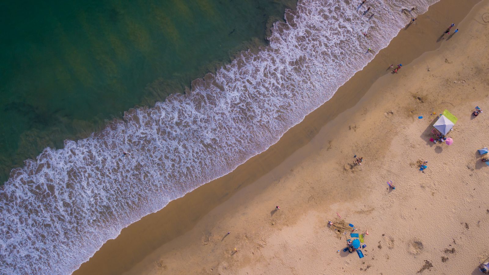 Aerial view of waves rolling onto a sandy beach on a sunny day