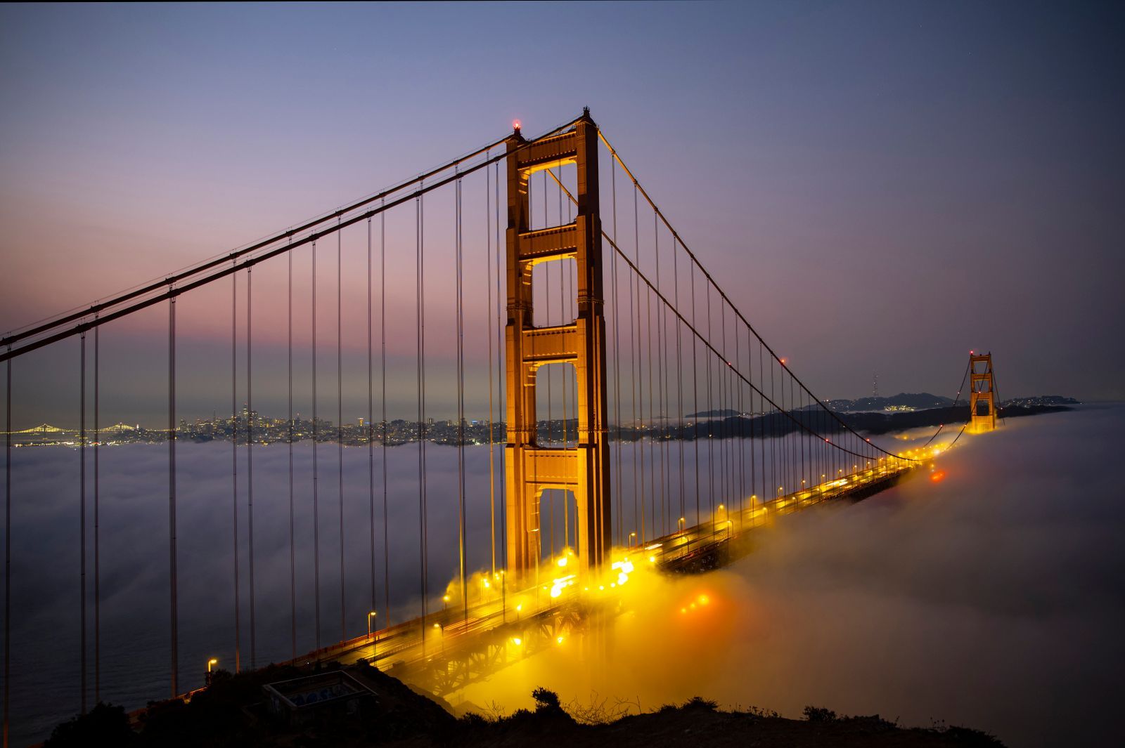 Golden Gate Bridge lit up at twilight above a blanket of fog